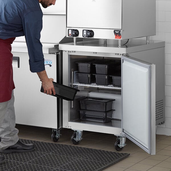 A man opening a white Avantco undercounter freezer with a silver handle.