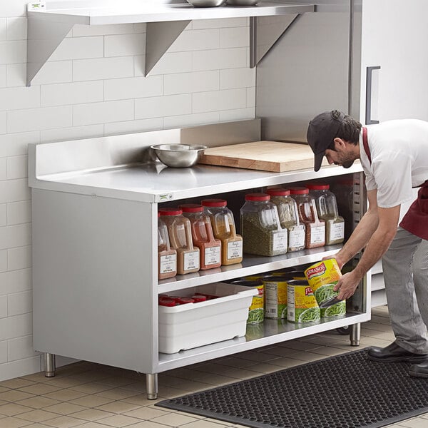 A man putting food on a Regency stainless steel shelf in a professional kitchen.