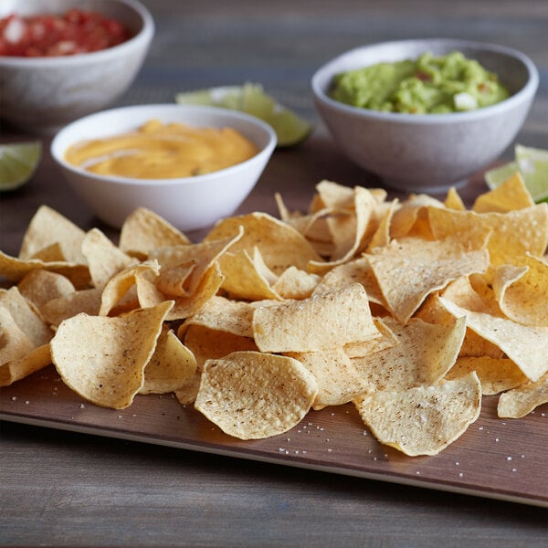 A plate of Mission 4-cut thin unfried tortilla chips with bowls of salsa and guacamole.