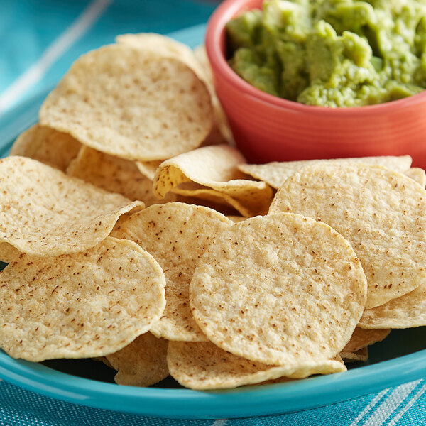 A blue plate with a bowl of Mission unsalted white round corn tortilla chips and guacamole.