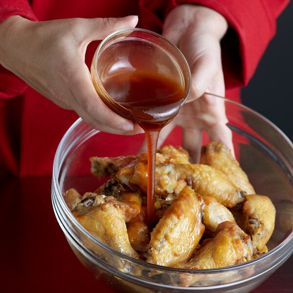 A person pouring Frank's RedHot Stingin' Honey Garlic Sauce onto a bowl of chicken wings.