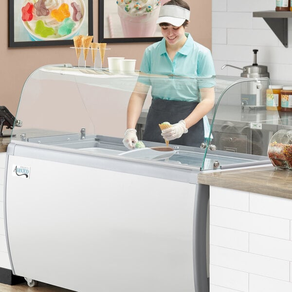 A woman in a blue shirt and white visor using an Avantco curved glass sneeze guard to put food in a bowl.