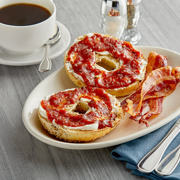 A plate with a bagel topped with TBJ Gourmet Spiced Tomato Jam and bacon.