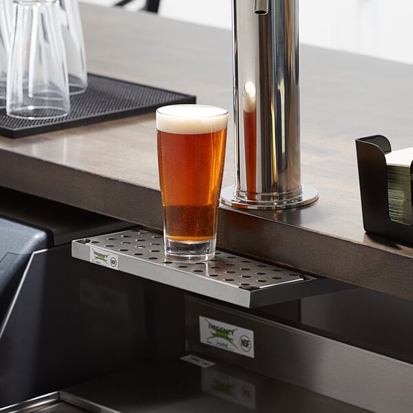 A glass of beer on a stainless steel bar drip tray.