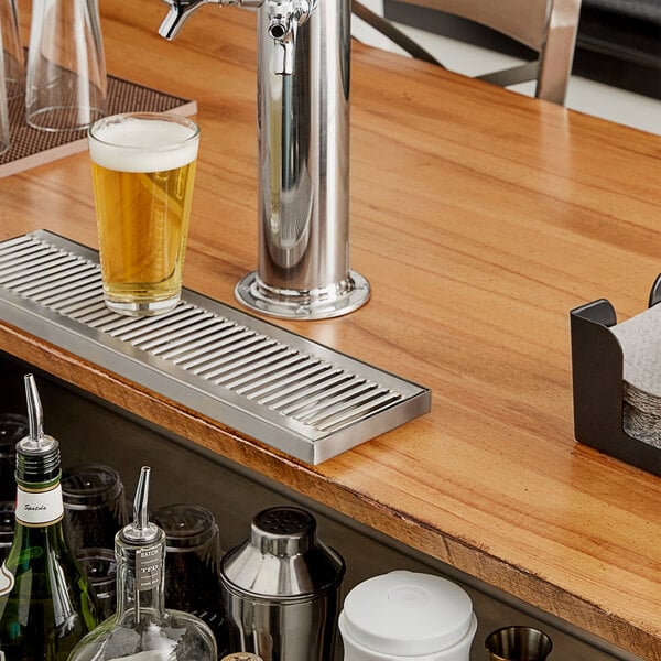 A Regency stainless steel beer drip tray on a counter with a glass of beer.
