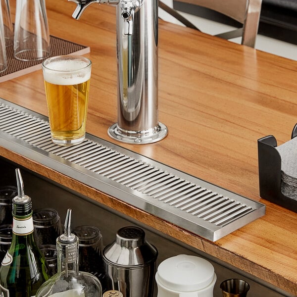 A Regency stainless steel surface mount beer drip tray on a counter with a glass of beer.