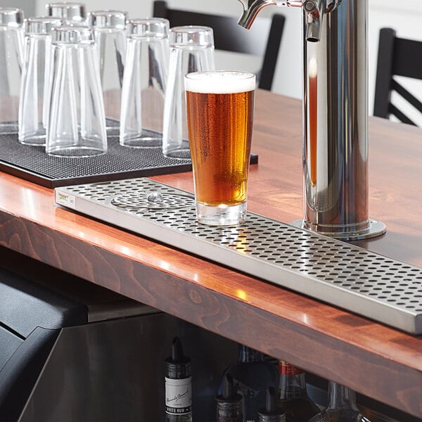 A Regency stainless steel beer drip tray on a metal bar with a glass of beer.