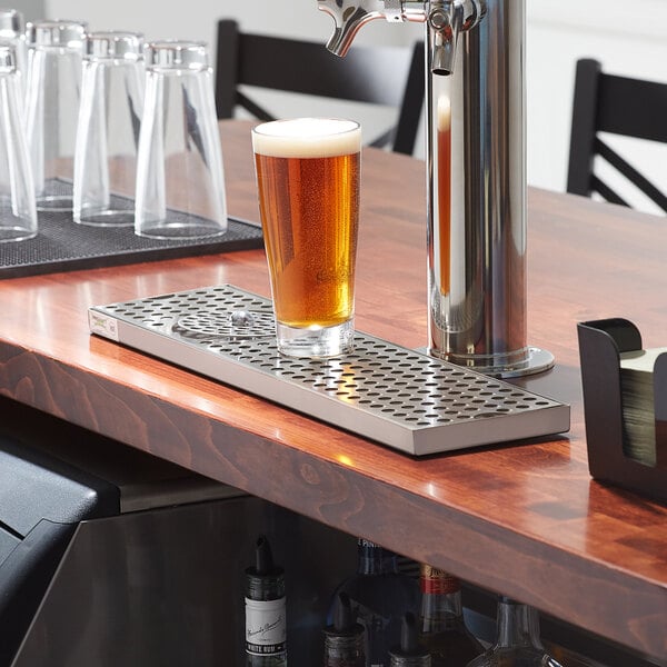 A Regency stainless steel beer drip tray with a glass of beer and water on a bar counter.