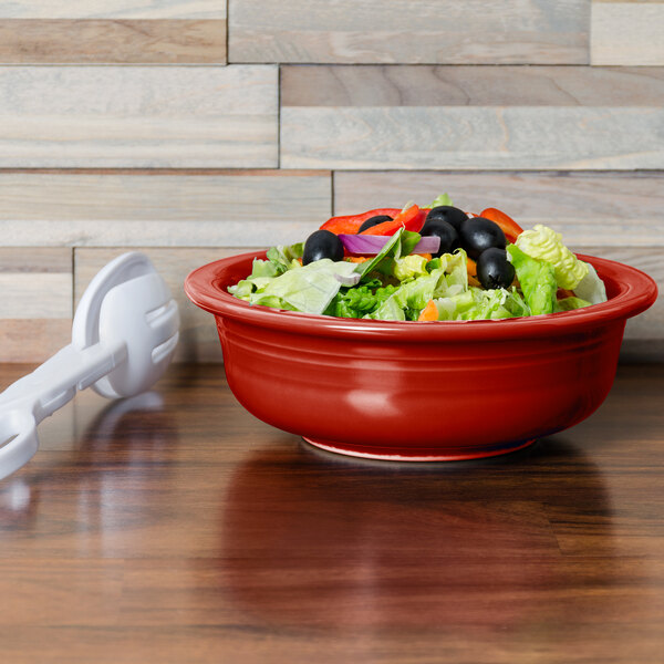 A red Fiesta serving bowl filled with salad on a wooden surface.