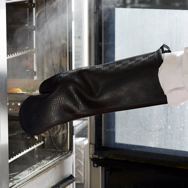 A person wearing a black San Jamar Flexguard silicone oven mitt.