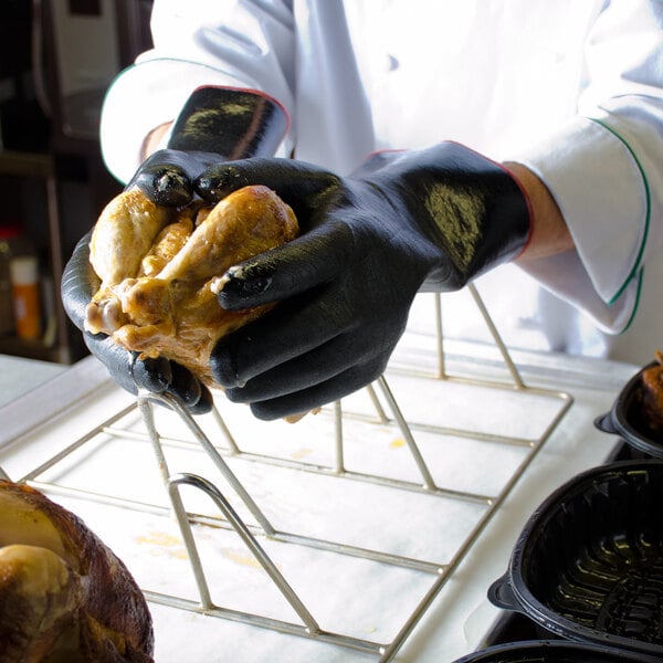 A person wearing San Jamar black neoprene gloves holds a cooked chicken.