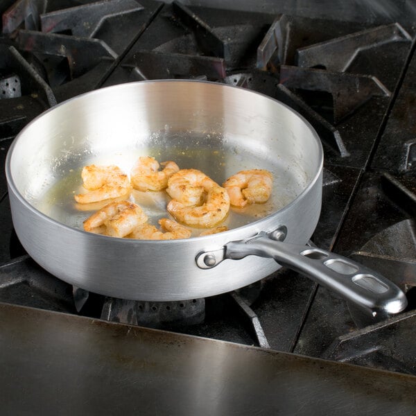 A Vollrath Wear-Ever saute pan with shrimp cooking on a stove.