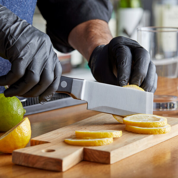 A person in black gloves using an Arcoroc by Chris Adams bar knife to cut lemons on a cutting board.