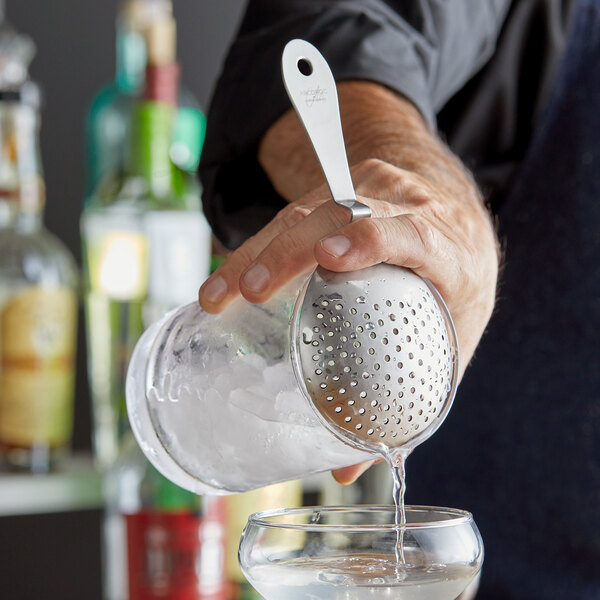 A person using an Arcoroc stainless steel Julep strainer to pour liquid into a glass.