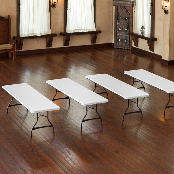 A group of Lifetime white rectangular plastic folding tables on a wood floor.