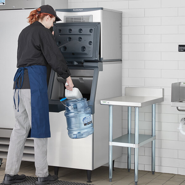 A person wearing a blue apron pouring water into a Scotsman air cooled ice machine.