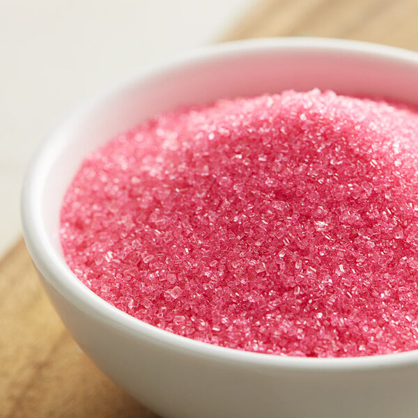 A bowl of Pink Sanding Sugar on a wooden table.