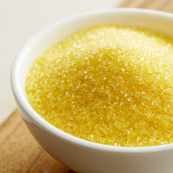 A bowl of yellow sanding sugar on a table.