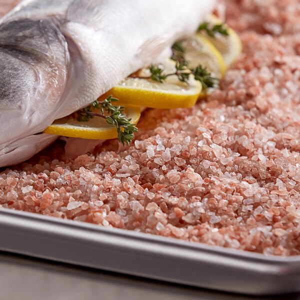 A fish on a tray of Regal pink Himalayan salt with lemon slices and herbs.