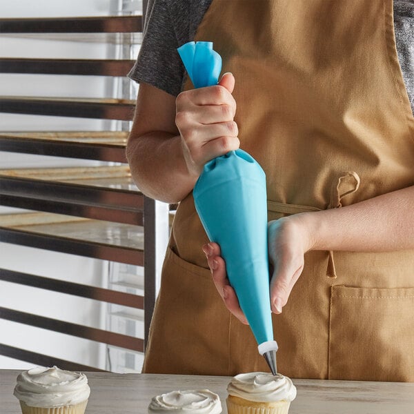 A woman in an apron using an Ateco blue reusable pastry bag to pipe white frosting on a cupcake.