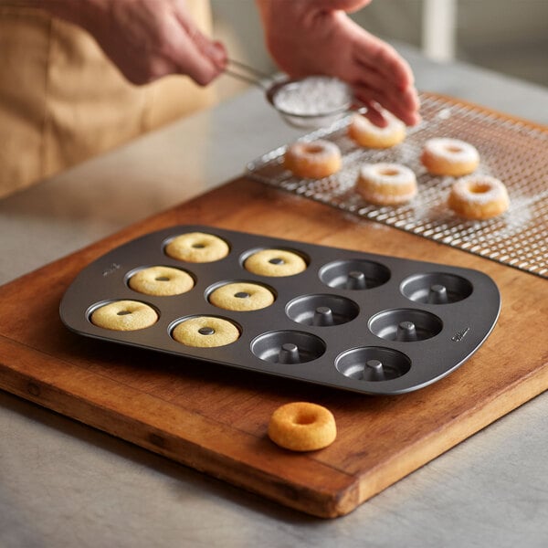A person putting doughnuts in a Wilton 12-cavity donut pan.