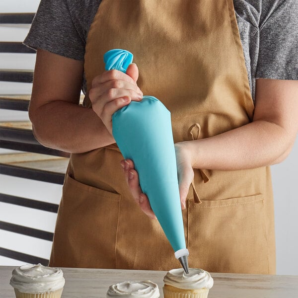 A person in an apron using an Ateco blue pastry bag to decorate cupcakes.