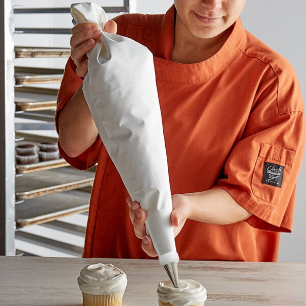 A person in an orange shirt using an Ateco polyurethane coated cotton pastry bag to frost a cupcake.