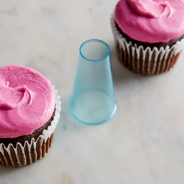 A cupcake with pink frosting and piped decorations using an Ateco plastic plain tip on a counter.