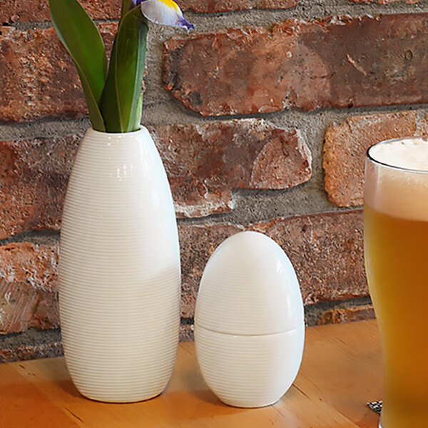 A white Front of the House bud vase with a flower next to a glass of beer.