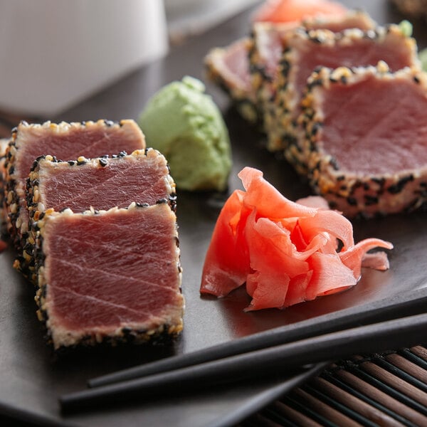 A plate of sliced tuna and pickled sushi ginger with chopsticks.