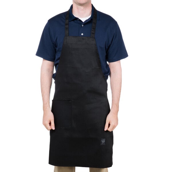 A man wearing a black Chef Revival bib apron with one pocket.