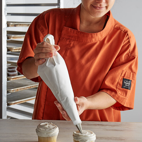 A woman in an orange shirt using an Ateco polyurethane coated cotton pastry bag to frost a cupcake.