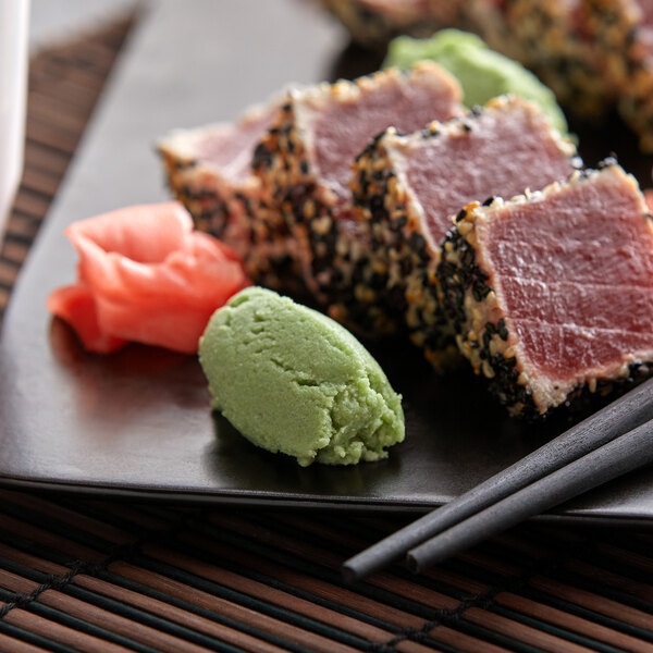 A plate of sushi with green tea and chopsticks on a table.