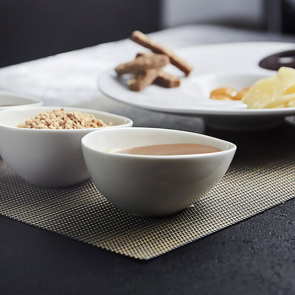 A plate with three vanilla bean porcelain bowls of brown liquid on a table.