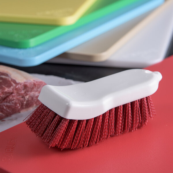 A white brush with red bristles sitting on a red cutting board.