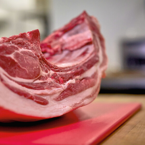 A piece of meat being cut on a red Vollrath cutting board.