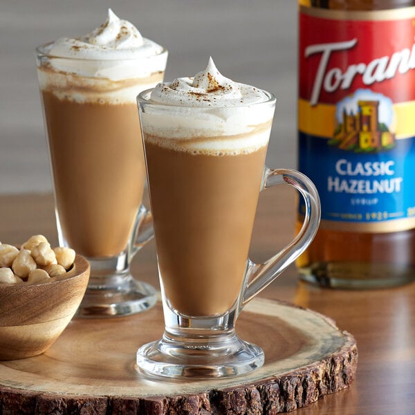 A glass of coffee with Torani Classic Hazelnut syrup and whipped cream with nuts on top.