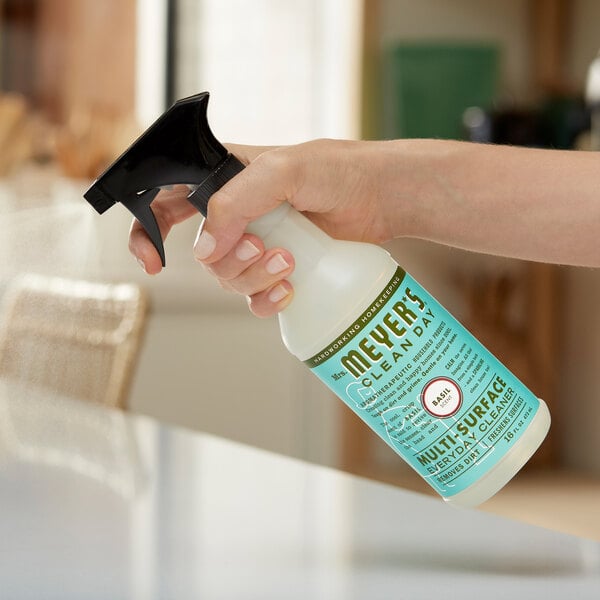 A hand holding a white spray bottle of Mrs. Meyer's Basil All Purpose Cleaner.