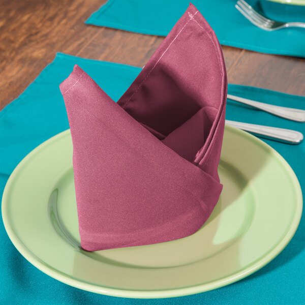 A folded mauve Intedge cloth napkin on a plate with a fork and knife.