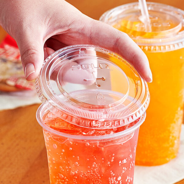 A hand holding a Solo plastic lid with a yellow drink in it.