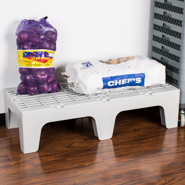 A Cambro slotted plastic shelf with a bag of potatoes and a bag of onions on it.