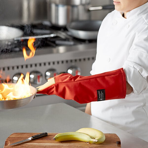 A chef using a San Jamar Cool Touch oven mitt to hold a pan with flames.