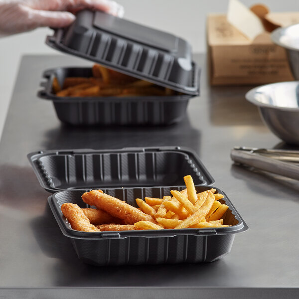 A person putting fried food in a black plastic Ecopax take-out container.