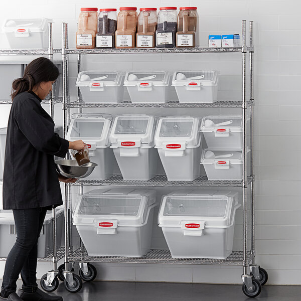 A woman standing in front of Rubbermaid ingredient bins on shelves in a school kitchen.