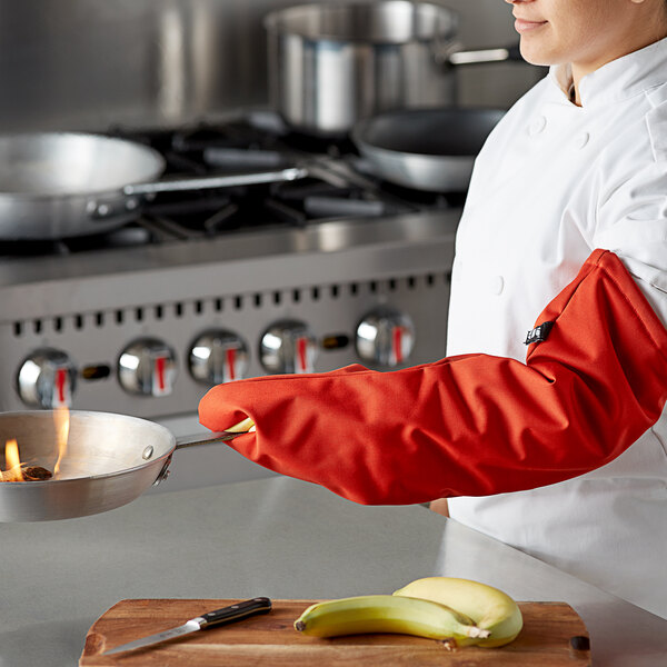 A woman in a chef's uniform using a San Jamar Cool Touch oven mitt to hold a hot pan.