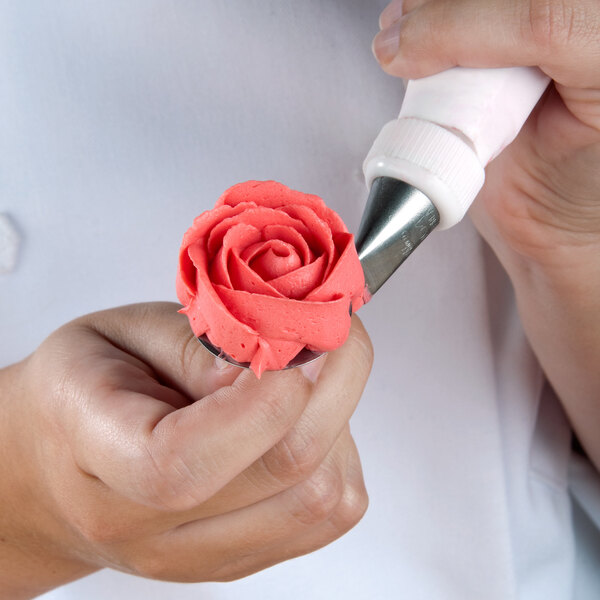 A person using an Ateco pastry bag to decorate a rose with a rose-shaped frosting tip.