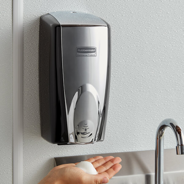 A person's hand using a Rubbermaid Autofoam soap dispenser over a sink.