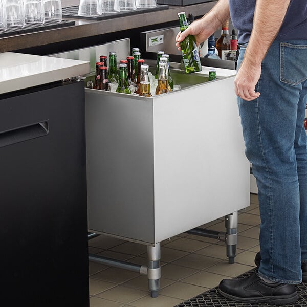A man putting a bottle into a Regency stainless steel beer cooler on a counter.