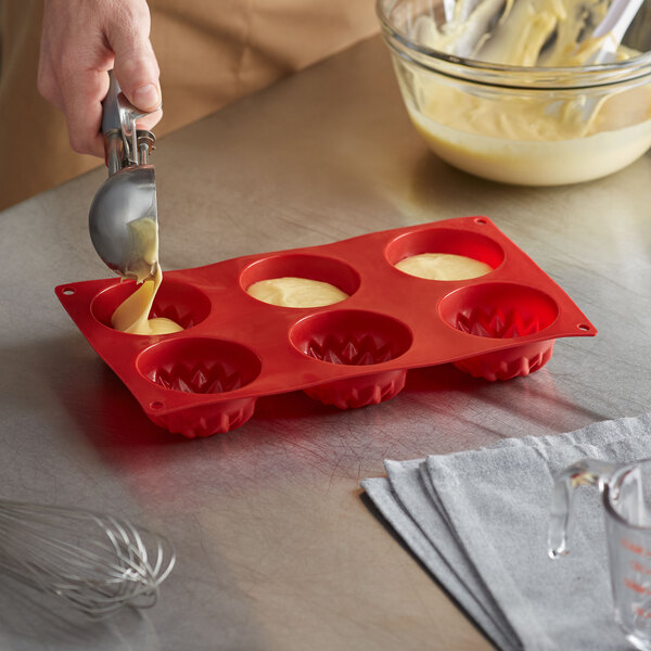 A person pouring batter into a Thunder Group red silicone sunflower mold.