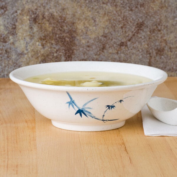 A white bowl of soup with a blue bamboo design on a table with a spoon.